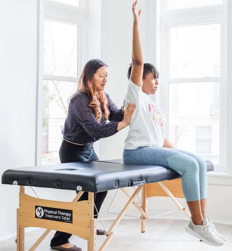 physical therapist evaluating a woman's shoulder pain on a treatment table in Arlington, Virginia