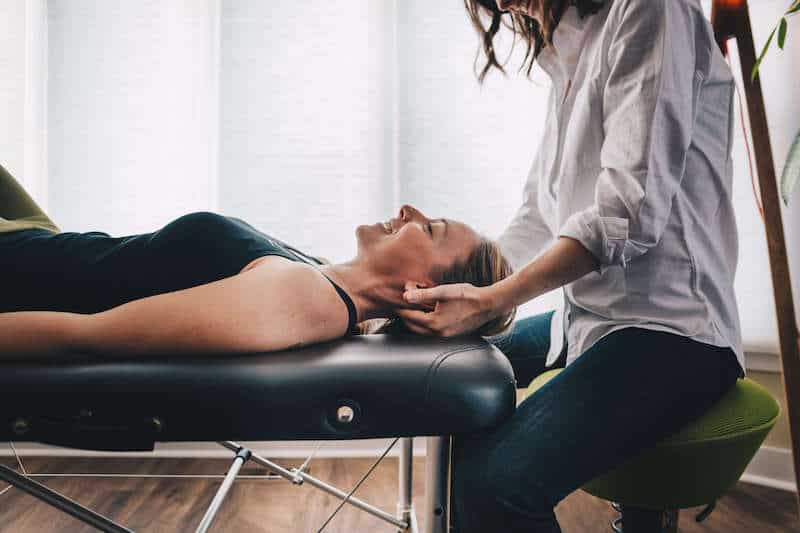 Physical therapist treating woman with neck pain with hands on therapy