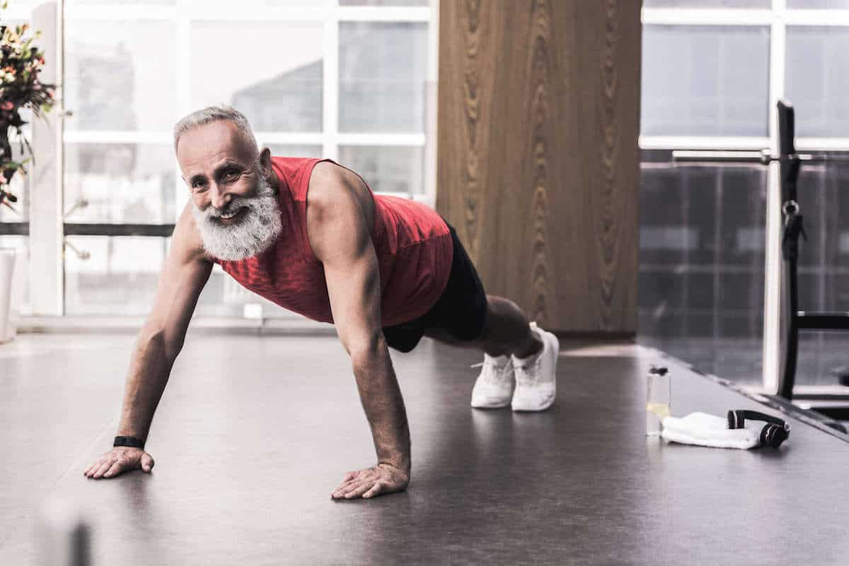 Older man with a beard at the gym doing a pushup