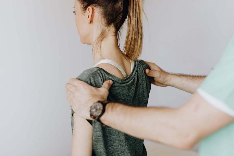 Physical therapist evaluating the posture of a woman with shoulder pain