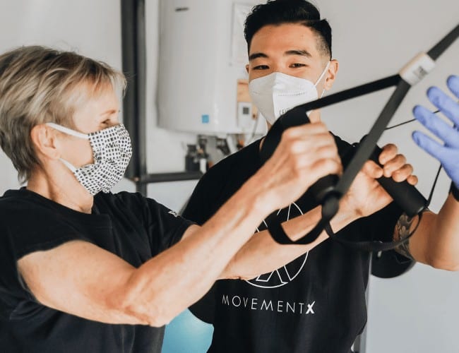 Physical therapist using a mask instructing patient on TRX exercises