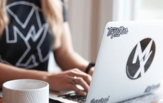 close up picture of woman typing on a laptop with Movement X sticker logo