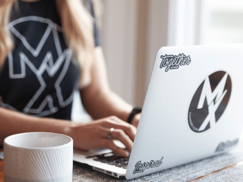 close up picture of woman typing on a laptop with Movement X sticker logo