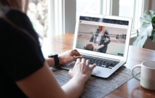 over the shoulder view of a woman typing on a laptop with the Movement X website on her screen