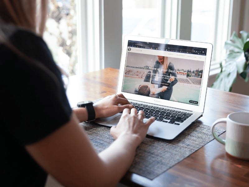 over the shoulder view of a woman typing on a laptop with the Movement X website on her screen