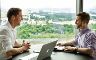 Movement X executives Scott and Josh sitting across from each other at a table with a skyline window view