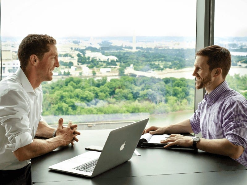 Movement X executives Scott and Josh sitting across from each other at a table with a skyline window view