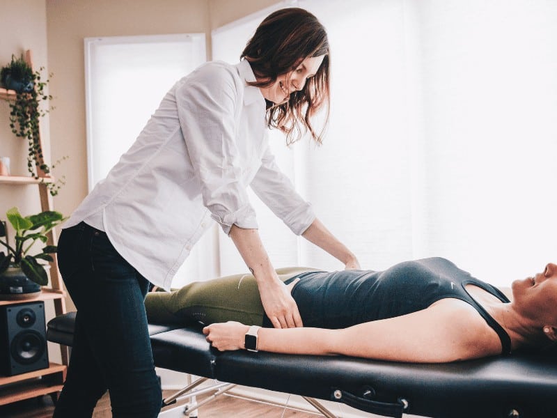 Physical therapist adjusting female patient on a medical mat table