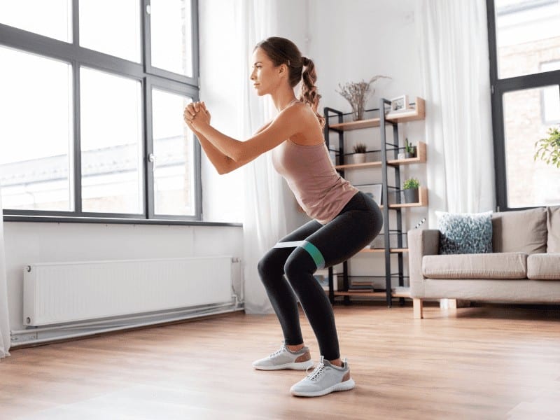 woman doing standing squats with a resistance band looped around her knees