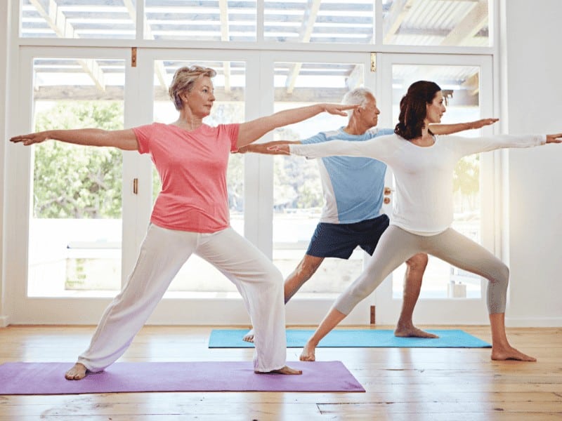 three older adults doing Warrior 1 yoga pose