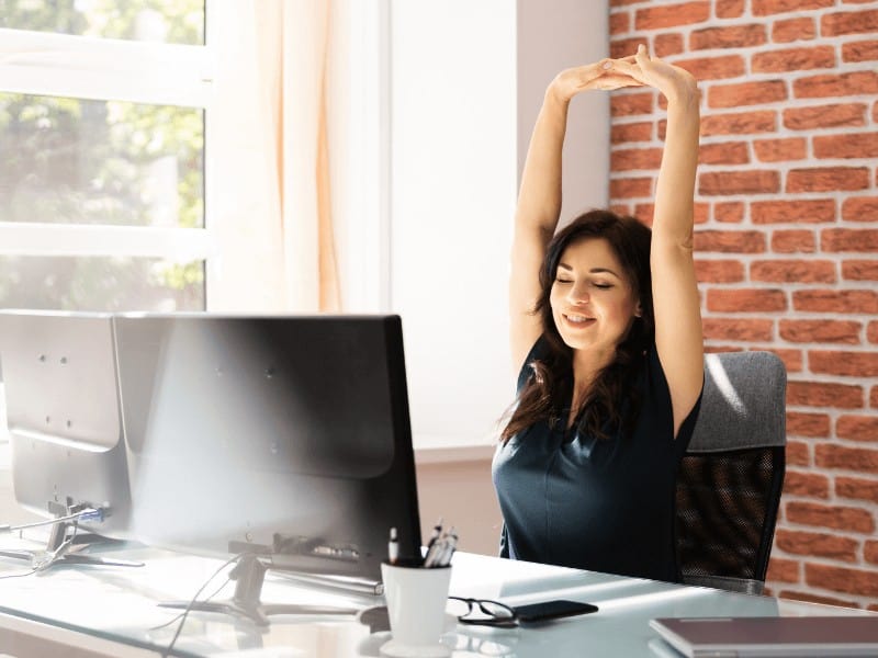 A female busy professional taking a stretching break from her desk at home while working from home
