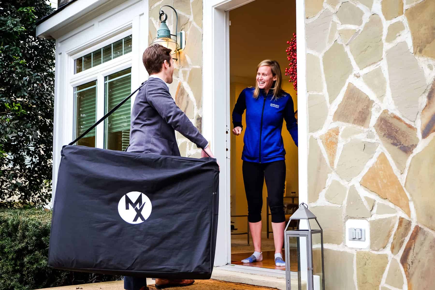 a movementx physical therapist being greeted at the door by one of his patients at their home while carrying a large portable treatment table