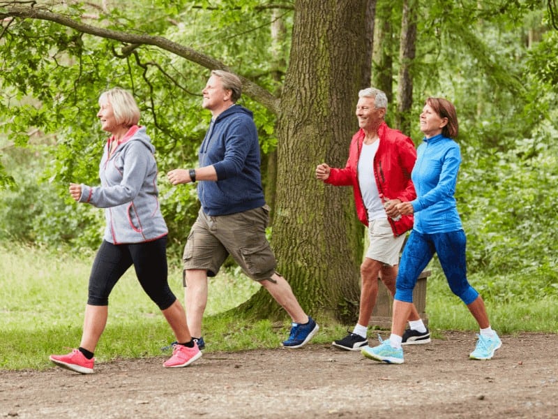 A group of active older adults enjoy walking exercise through a park on a nice day
