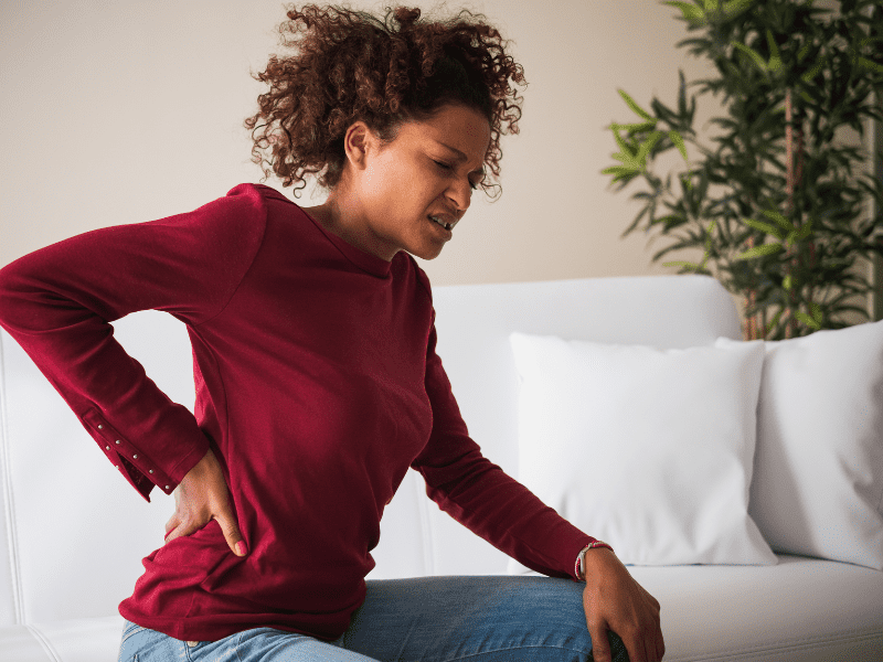woman sitting on the couch grabbing her back in pain with a painful expression because of a disc herniation in her spine