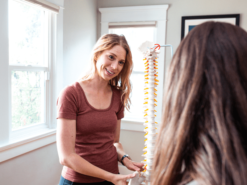 physical therapist demonstrating an anatomical model of a spine to a patient with spinal stenosis pain