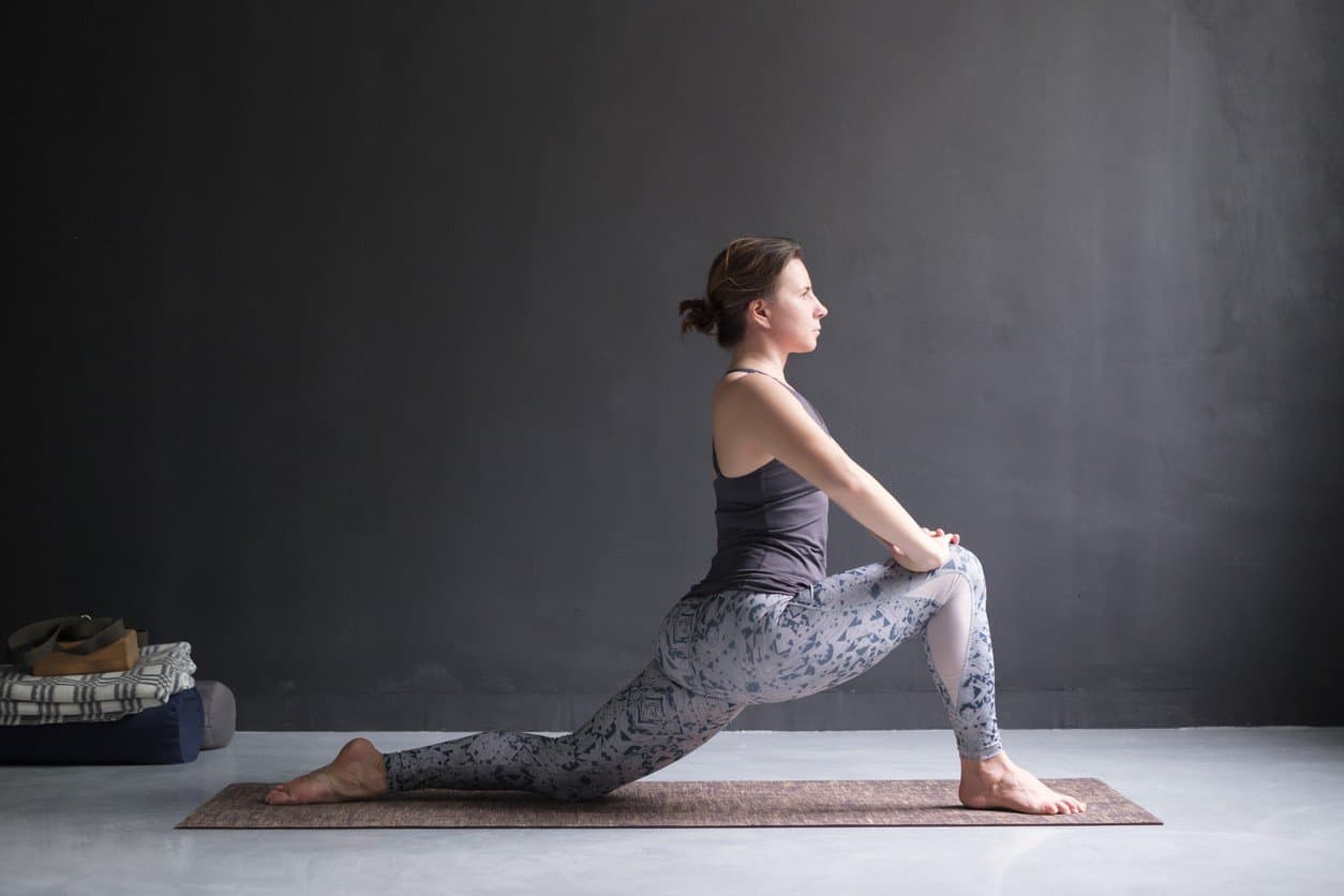 woman performing a hip flexor stretch yoga pose to improve her running form mechanics