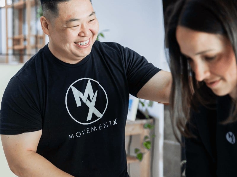 MovementX physical therapy in portland provider Dr. Steven Park wearing a black movementx physical therapist shirt smiling while helping a patient get stronger during a physical therapy appointment at home