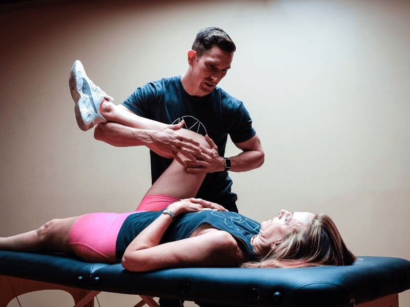 MovementX physical therapist in Orange County Chris Monpere mobilizing the hip joint on a patient with hip pain from a sports injury on a black treatment table