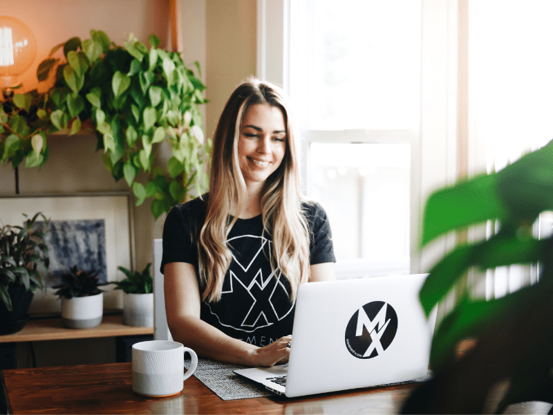 A female physical therapist with MovementX physical therapy hosting a virtual telehealth PT session on her laptop with a patient seeking remote physical therapy with a cup of coffee on the table and bright morning light