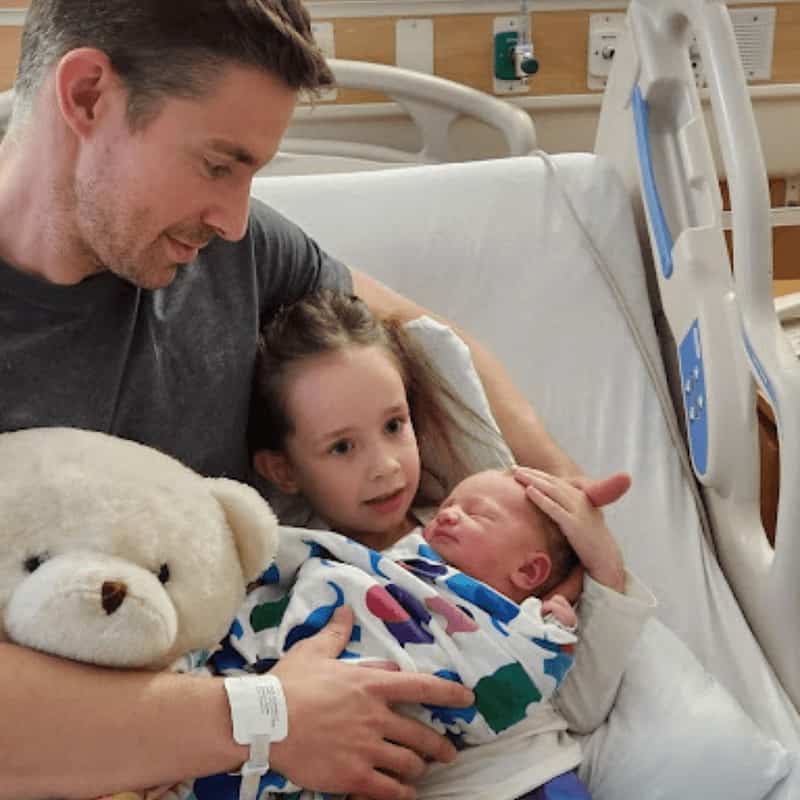 MovementX physical therapist Dr. Dan Alcorn, PT, DPT holding his new born son in the hospital with his daughter and a teddy bear