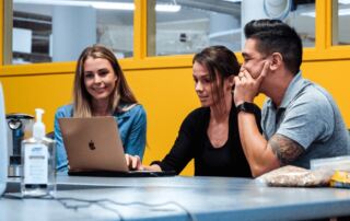 Three MovementX colleagues working together at their headquarters solving problems on their laptop