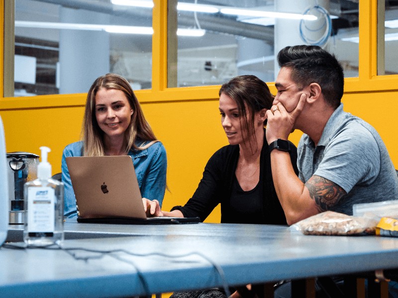 Three MovementX colleagues working together at their headquarters solving problems on their laptop