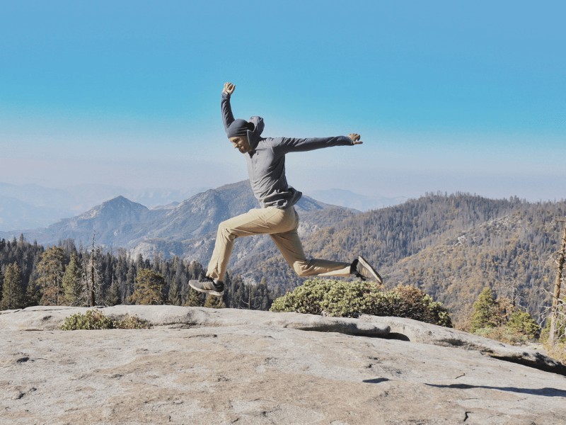 A MovementX physical therapy provider jumping with arms stretched on top of a rocky outcropping.