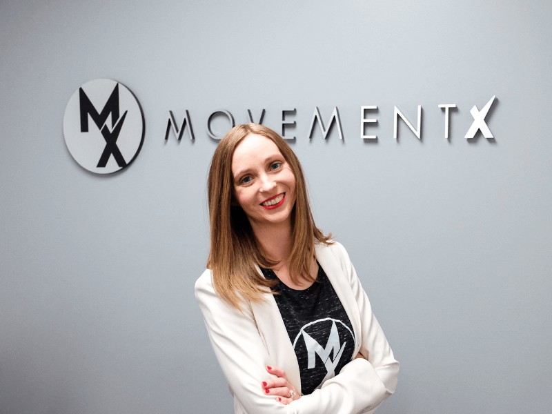 Dr. Stephanie Weyrauch, PT, DPT standing in front of a MovementX sign in her practice in Billings, Montana.