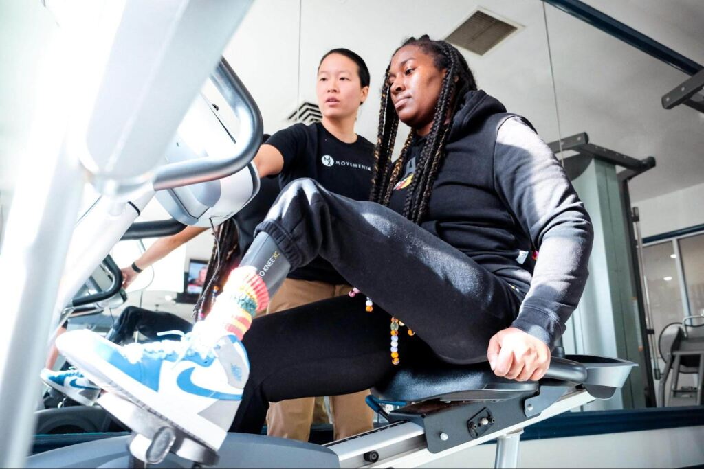 Dr. Audrey Chien coaching a limb loss patient while they ride on a stationary recumbent bicycle during a physical therapy session in Columbia, Maryland.