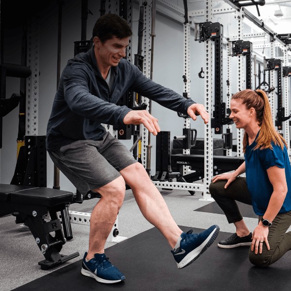 A movementx sports physical therapy helping an athlete with plyometric jumping exercises for single leg strength in a gym setting.