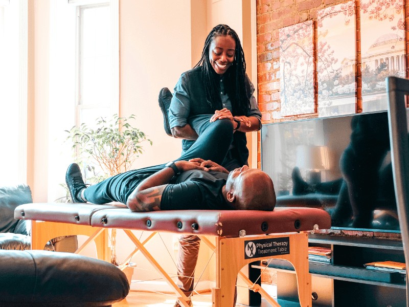 Physical therapist conducting a home visit to help a male athlete with recovery exercises in a living room setting.