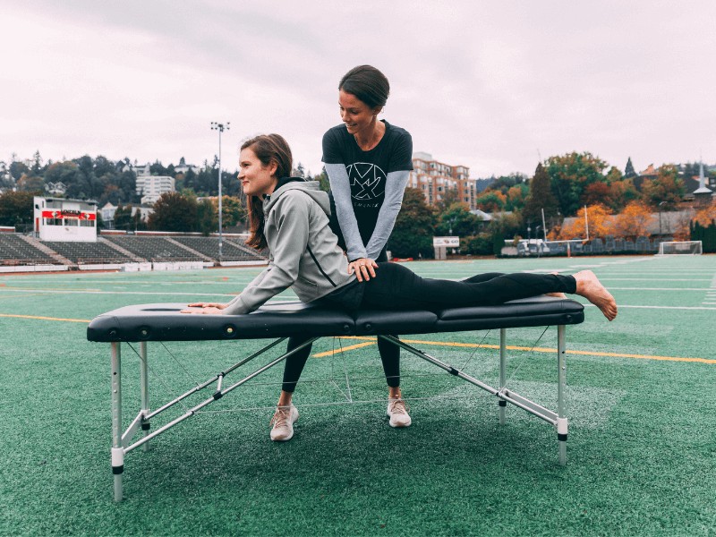 Physical therapist treating a female track athlete on an outdoor track.