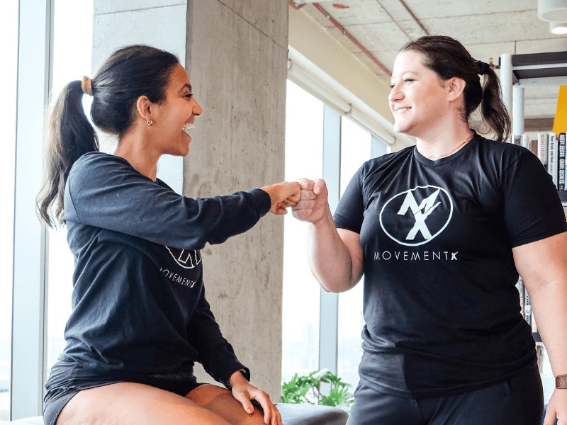 A movementx sports physical therapist fist bumping in celebration with a runner athlete after a successful PT plan.