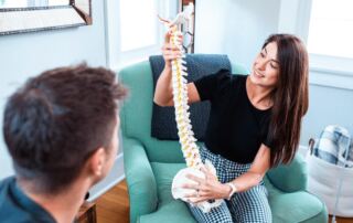 Dr. Mikaila Boldt, PT, DPT demonstrating elements of a spinal column on a model while seated with a patient.