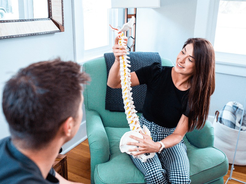 Dr. Mikaila Boldt, PT, DPT demonstrating elements of a spinal column on a model while seated with a patient.