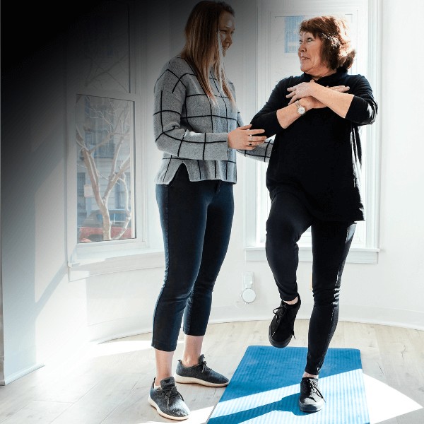 A MovementX neuro physical therapist assisting a patient with Parkinson's disease through balance training exercises using a blue balance pad.