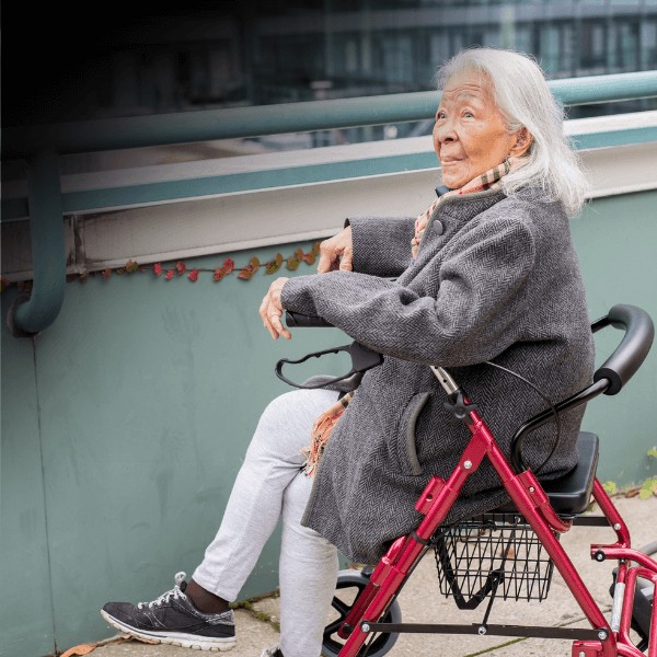 An elderly woman enjoying a nice view while seated in a red walker outside.