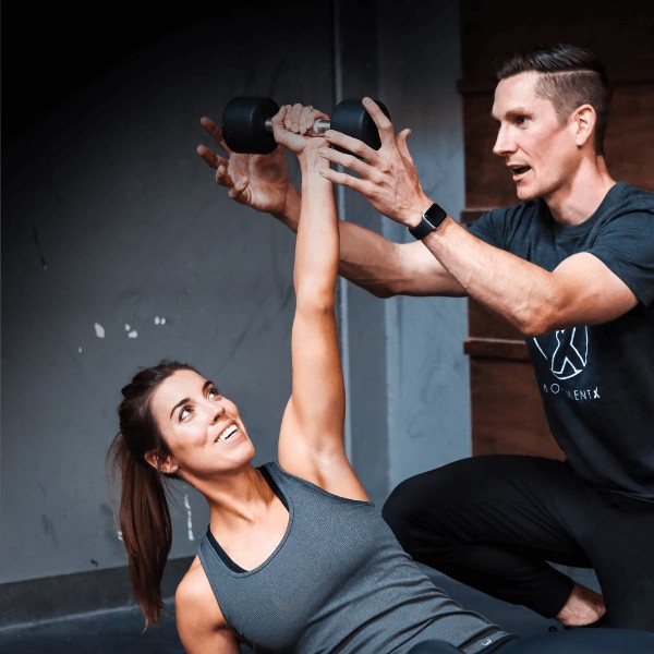 A MovementX orthopedic physical therapist guiding a female patient through personalized strength training exercises using a dumbbell to build muscle strength and meet fitness goals.