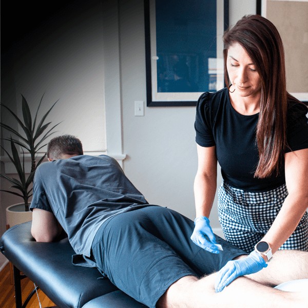 A female MovementX orthopedic physical therapist performing dry needling to relieve calf muscle knots and tension areas for deep pain relief in a home setting.