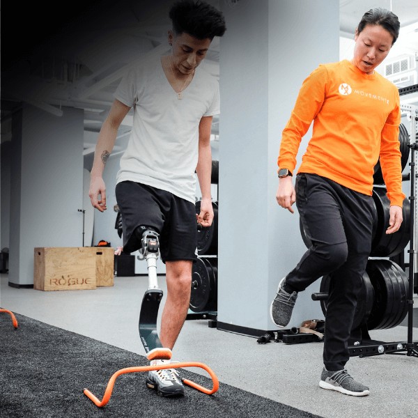 A MovementX orthopedic physical therapist guiding an amputee patient with a lower leg amputation through gait training techniques in a gym setting.