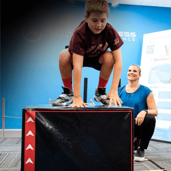 A MovementX pediatric physical therapist helping a young athlete improve performance with sports-specific training to build agility and endurance on a large box jump.