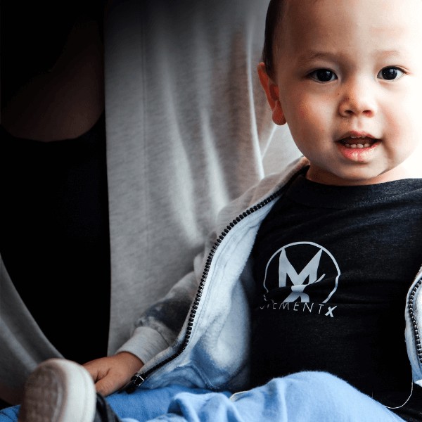 A young child smiling at the camera wearing a MovementX shirt.