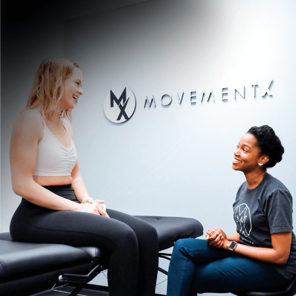 A MovementX vestibular physical therapist talking about preventing dizziness, headaches, and vertigo with a patient in a clinic setting with a MovementX logo on the wall behind them.