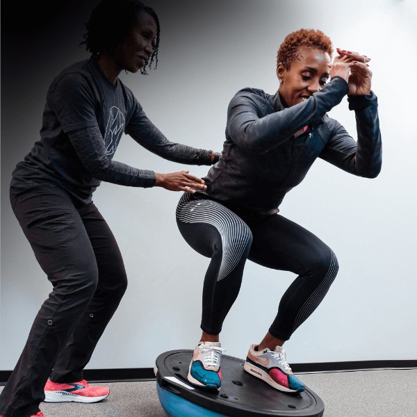 A movementx vestibular physical therapist working with a patient on balance while squatting low on a BOSU ball against a white background