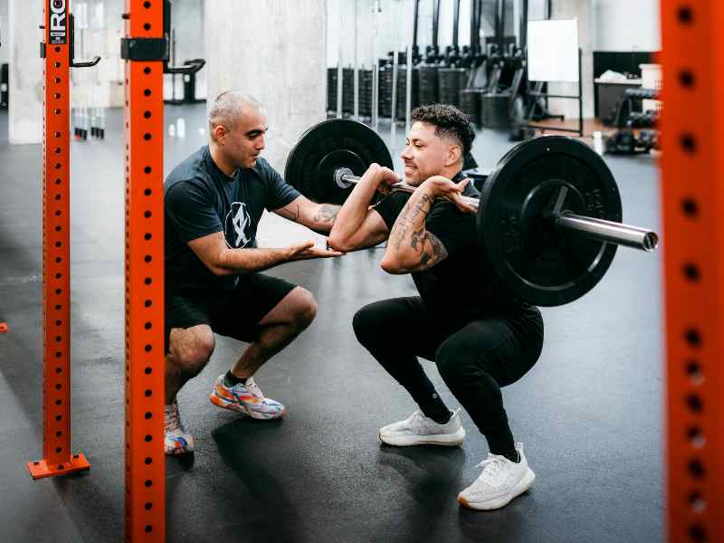 Romin Ghassemi, PT, DPT helping a patient work on squat stability during a front squat in a gym's power rack.