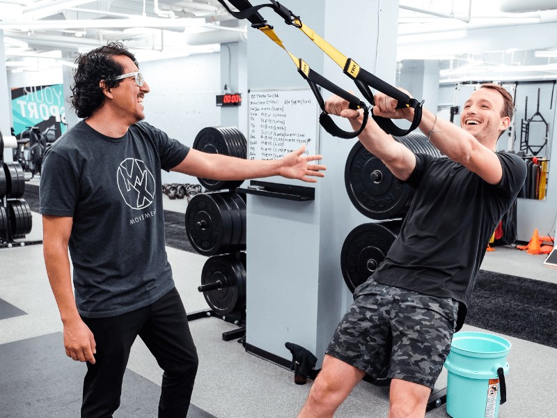 a movementx personal trainer working with a male client in a gym setting on strengthening and conditioning