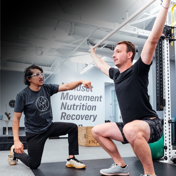 a movementx personal trainer working on strength during a squat lifting exercise in a bright gym setting