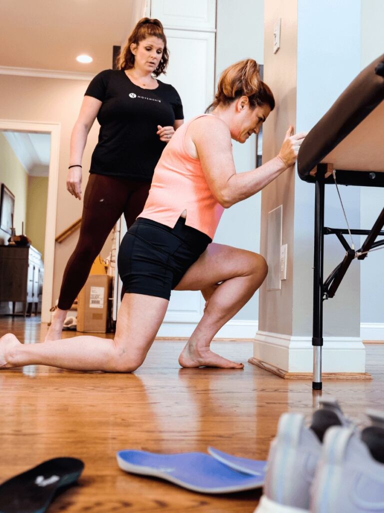 Meg Pezzino, PT, DPT helping a runner stretch against a wall in their home during a physical therapy session.