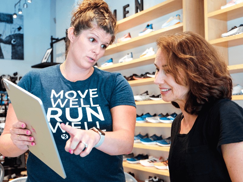 Meg Pezzino, PT, DPT showing a runner a demo of how they might perform after physical therapy in a running store.