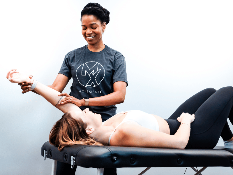 A MovementX physical therapist laughing with a patient while they work through shoulder mobility exercises on a treatment table.